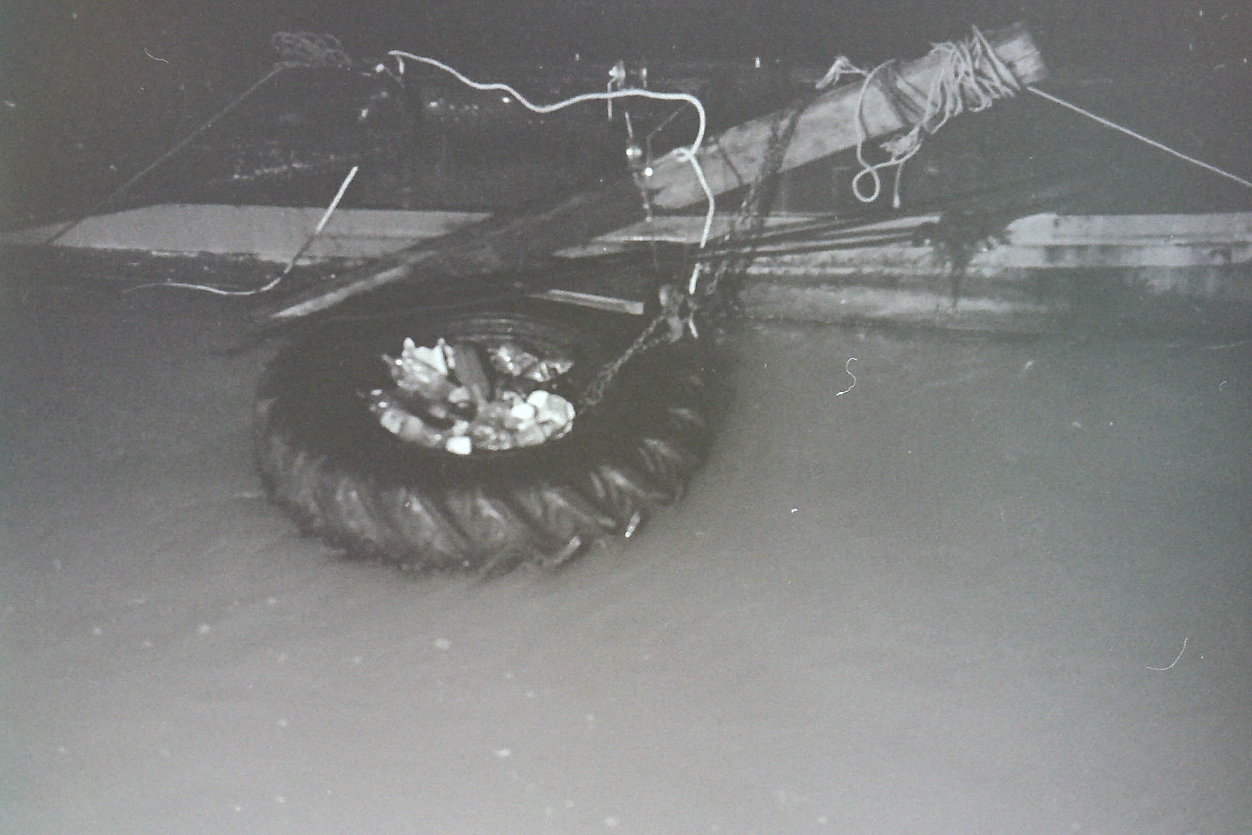 planches de bois, fils de fer et pneu de tracteur flottant dans la crue de la seine à paris dans la nuit en noir et blanc
