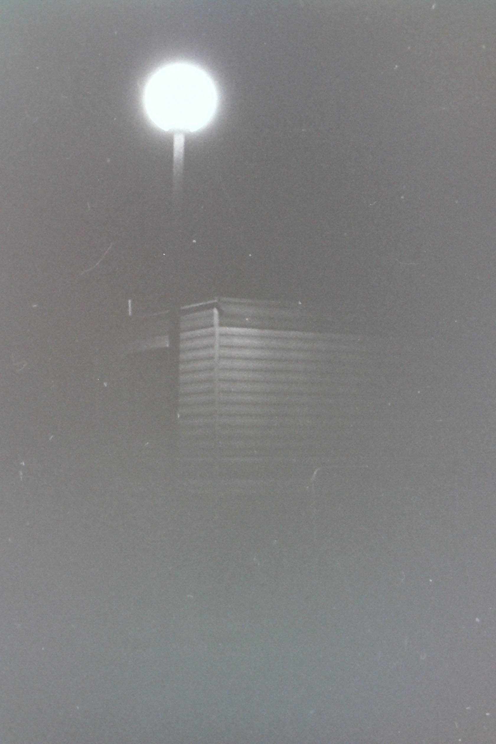cabane en tôle mystérieuse éclairée par un lampadaire rond dans la nuit en noir et blanc