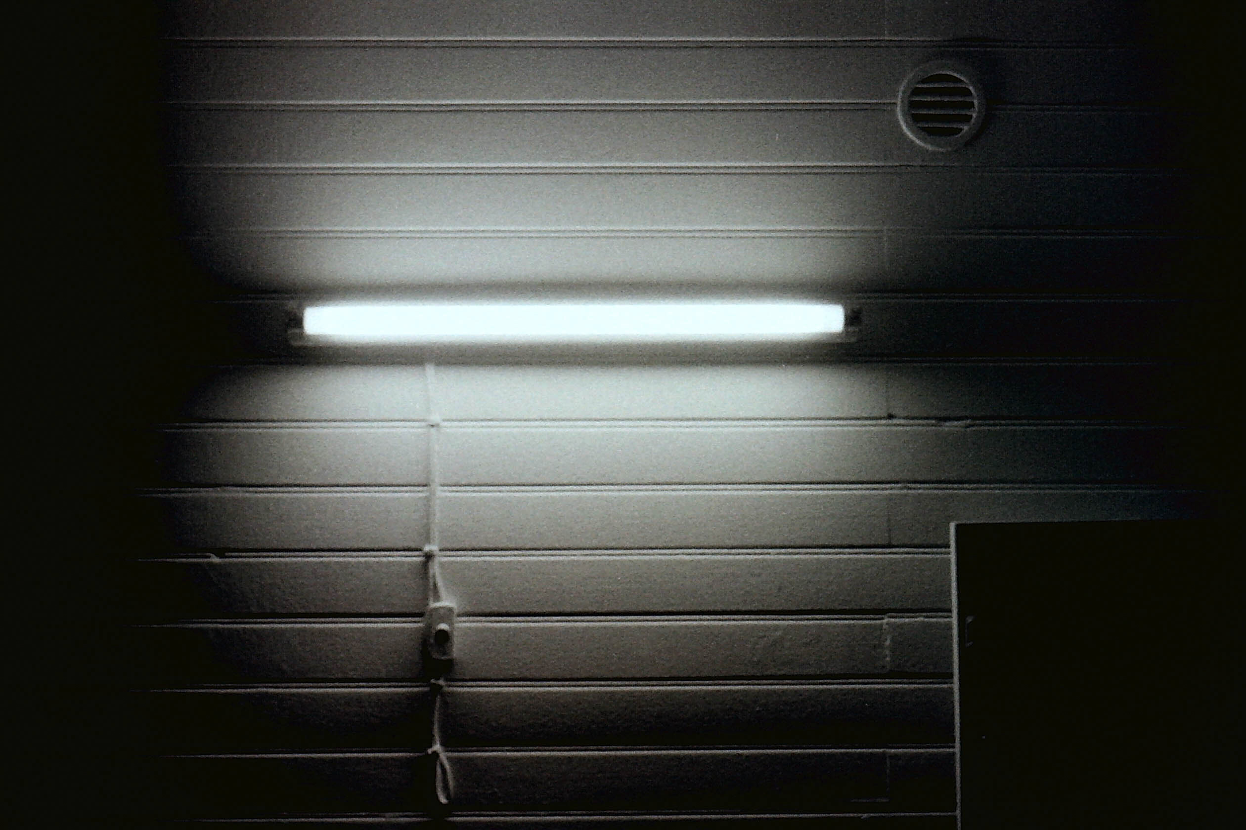 néon sur mur de lambris blanc avec interrupteur, cable et bouche d'aération dans la nuit en noir et blanc
