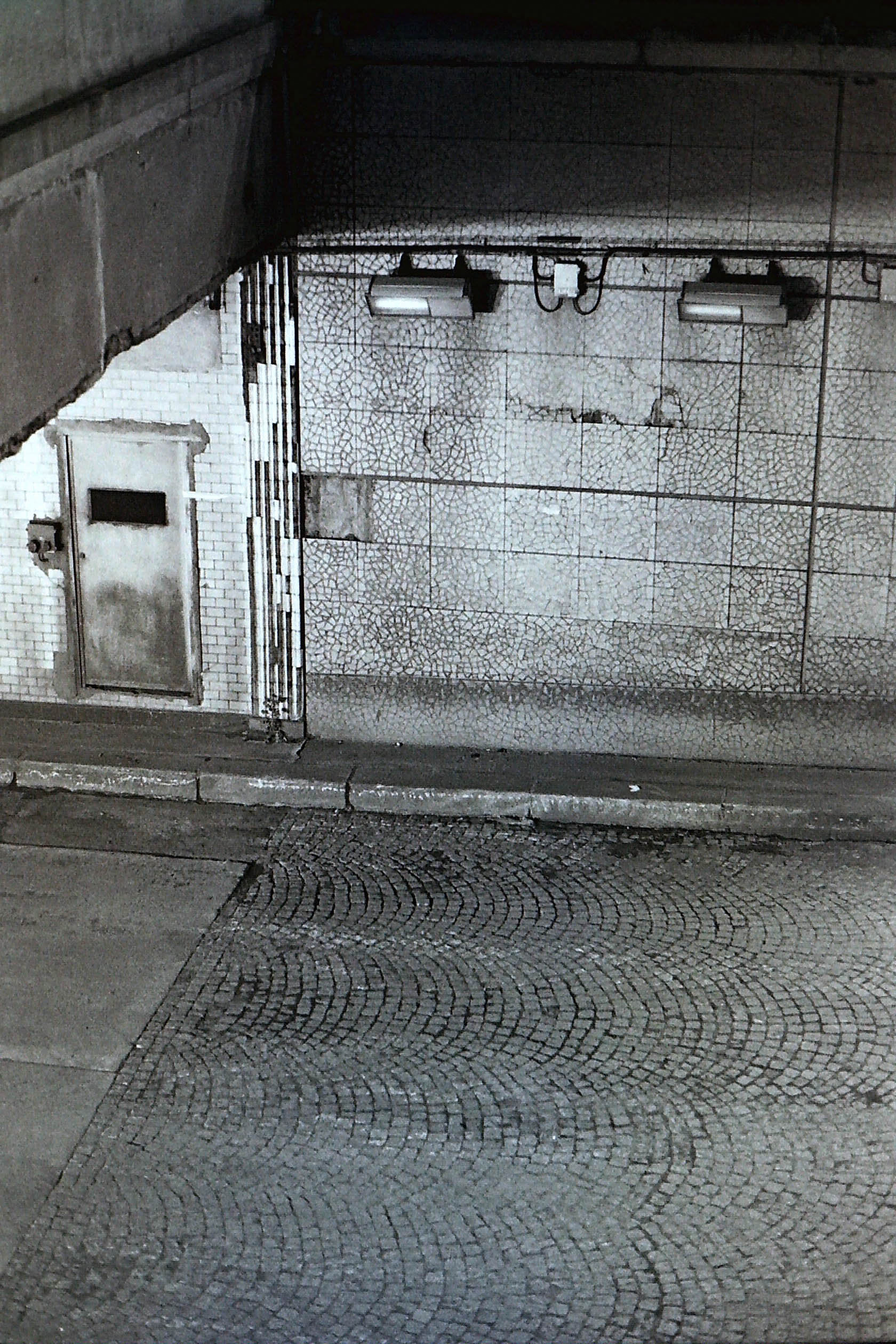 porte métallique sur mur sous un pont devant une rue pavée de paris avec spotlight dans la nuit en noir et blanc